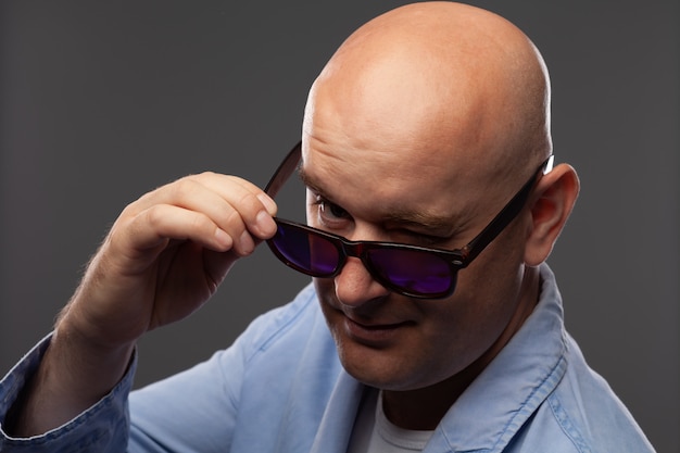 Homme chauve à lunettes noires sur un mur gris