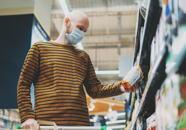 Un homme chauve en masque médical choisit des produits dans le supermarché, concept de quarantaine de coronavirus