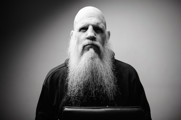 Homme chauve mature avec une longue barbe grise contre un mur blanc en noir et blanc