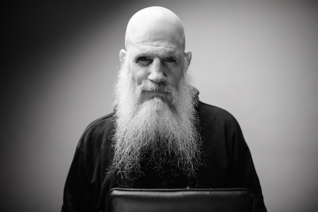 Homme chauve mature avec une longue barbe grise contre un mur blanc en noir et blanc