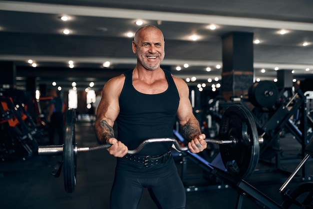 Homme chauve musclé travaillant dans une salle de gym faisant des exercices avec haltères au concept de musculation biceps