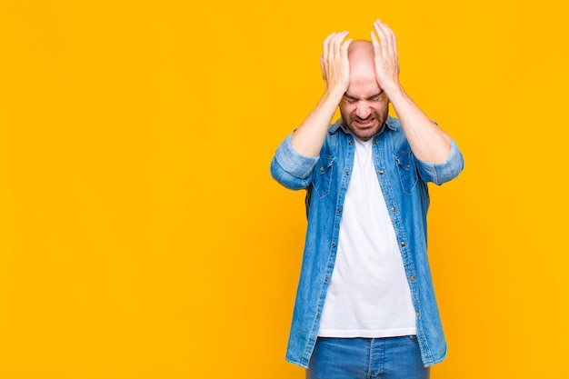 Homme chauve se sentant stressé et anxieux, déprimé et frustré par un mal de tête, levant les deux mains à la tête