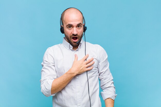 Homme chauve se sentir choqué, étonné et surpris, avec la main sur la poitrine et la bouche ouverte