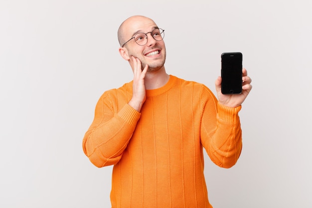 Homme chauve avec un smartphone contre un mur isolé