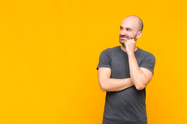 Homme chauve souriant joyeusement et rêvassant ou doutant, regardant sur le côté