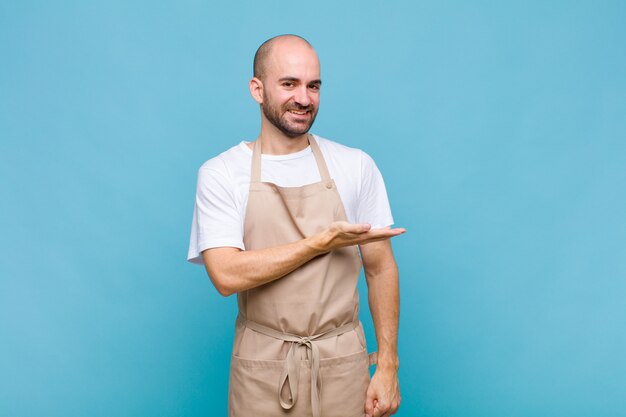 Homme chauve souriant joyeusement, se sentir heureux et montrant un concept dans l'espace de copie avec la paume de la main