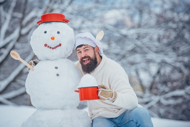 Homme de chef de Noël avec bonhomme de neige dans la cuisine d'hiver beau cuisinier du père noël