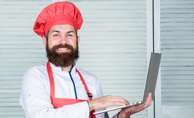 Homme chef à la recherche d'ingrédients en ligne cuisiner des aliments Épicerie en ligne Service de livraison Ordinateur portable du chef à la cuisine École culinaire Hipster en chapeau et tablier acheter des produits en ligne Achats en ligne