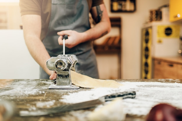 Homme chef en tablier travaille avec machine à pâtes