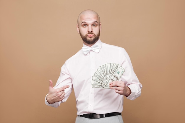 Homme en chemise blanche debout tenant et pointant du doigt plusieurs dollars en main et regardant la caméra