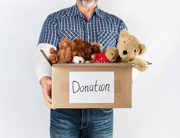 Un homme en chemise bleue et jeans tenant une grande boîte de papier brun avec des jouets pour enfants