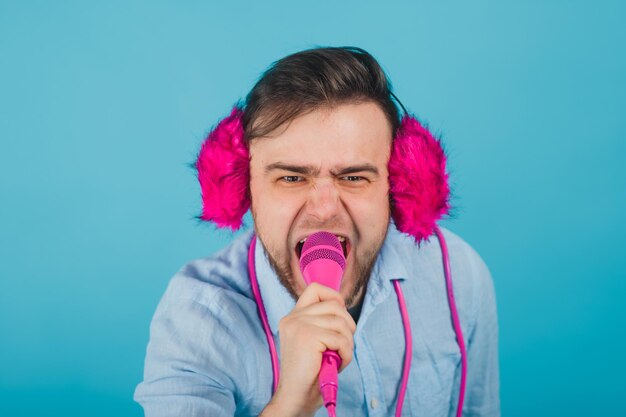 l'homme en chemise bleue se tient sur fond bleu dans un casque rose et chante dans un microphone rose