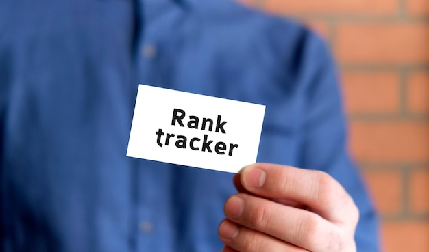 Un homme en chemise bleue tient une pancarte avec le texte de Rank tracker dans une main