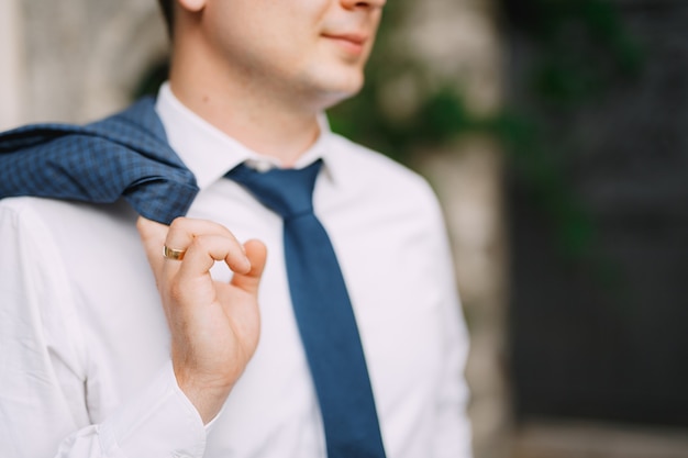 Un homme en chemise et cravate tient une veste sur son épaule, gros plan