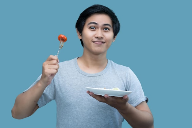 Photo un homme en chemise grise tient une fourchette et une assiette contenant de la nourriture pour la conception et l'édition visuelle