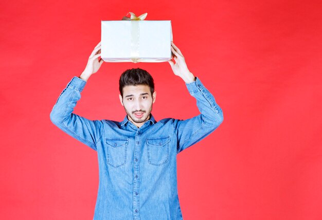 Homme en chemise en jean tenant une boîte cadeau en argent.