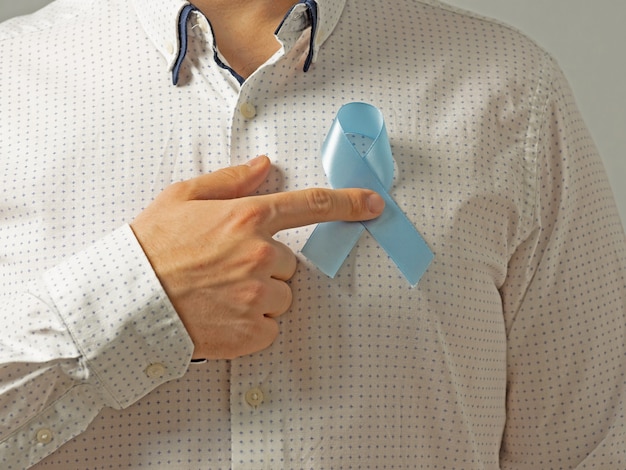 Un homme en chemise légère tient près du cœur un ruban bleu, symbole de la sensibilisation au cancer de la prostate. Concept de médecine et moyens de soins de santé