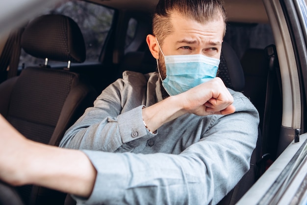 homme en chemise et masque médical est assis au volant de la voiture.