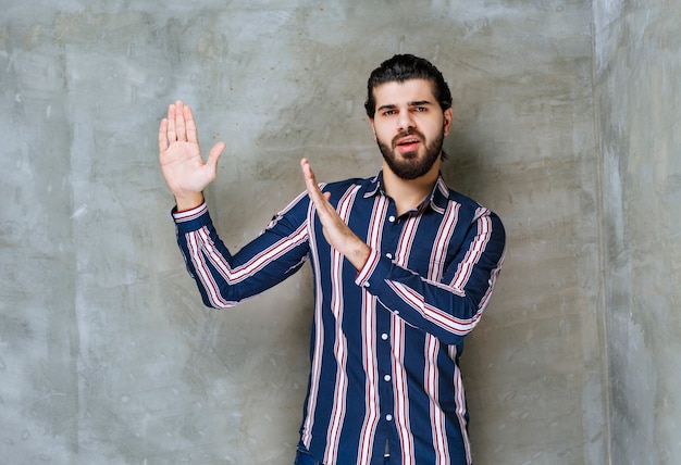 Homme en chemise rayée ouvrant la main et refusant.