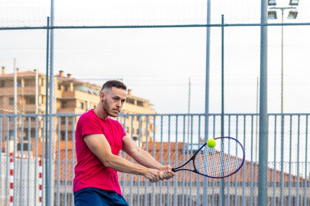 Un homme en chemise rouge joue au tennis avec une balle jaune.