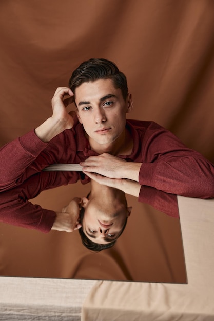 Un homme en chemise à une table avec un miroir et des reflets sur un fond de tissu Photo de haute qualité