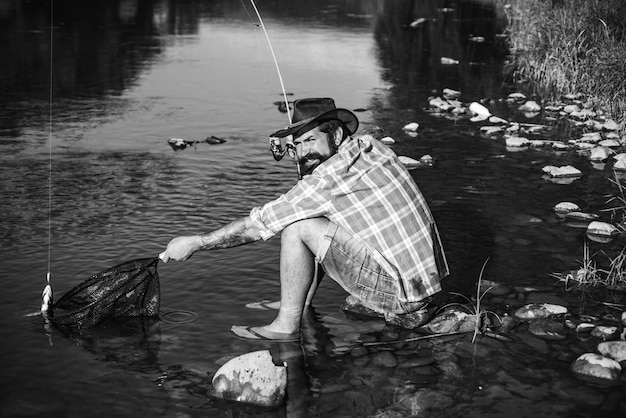 Homme en chemises pêchant avec filet et tige pendant la lumière du matin sur le lac poisson sur crochet poisson pêcheur