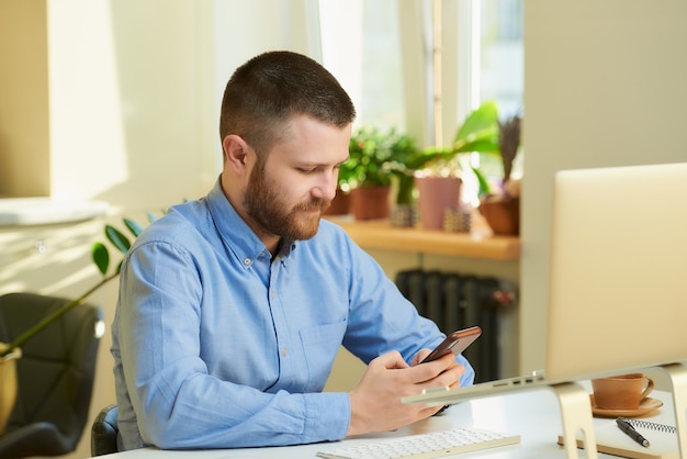 Un homme cherche des nouvelles sur Internet sur un smartphone devant un ordinateur portable.