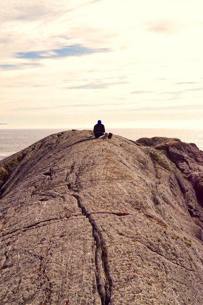 Un homme avec un chien assis sur un rocher contre le ciel