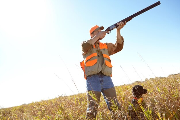 Homme et chien avec fusil à l'extérieur pour la chasse, moniteur, parc et recherche de danger ensemble dans la nature, personne mature, animal de compagnie et aidant de chasseur sur le terrain pour guider dans les bois, maquette et équipe de suivi