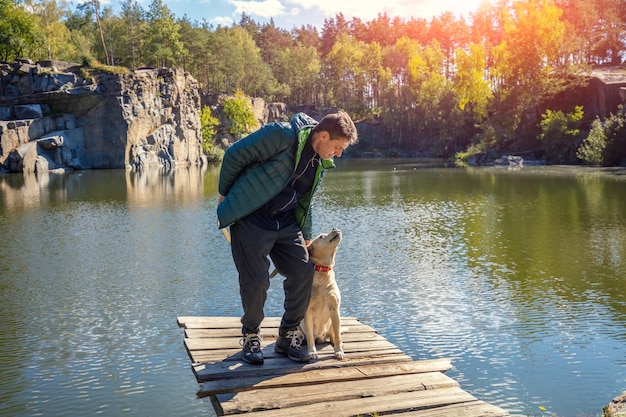 Un homme avec un chien Labrador retriever se dresse sur une terrasse en bois au bord du magnifique lac de granit