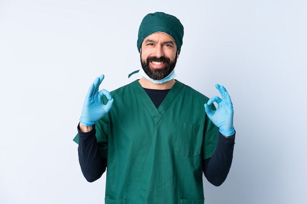 Homme chirurgien en uniforme vert sur mur isolé montrant signe ok avec les deux mains