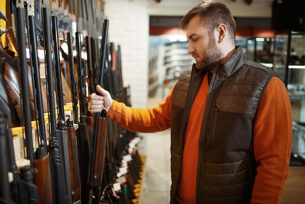Homme choisissant le fusil à la vitrine dans le magasin d'armes à feu.