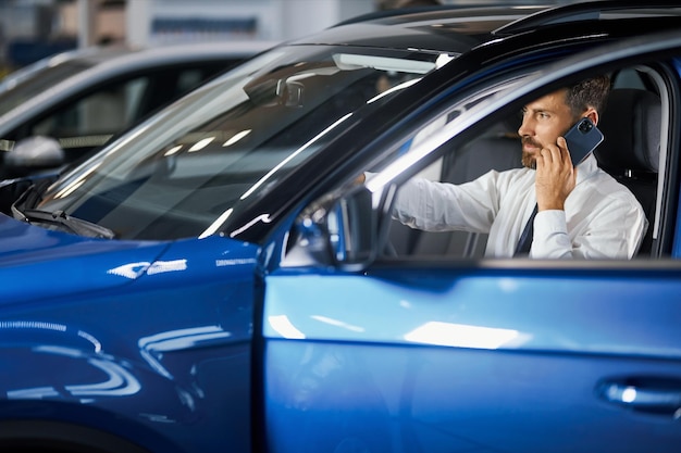 Homme choisissant une voiture et parlant sur mobile dans la salle d'exposition