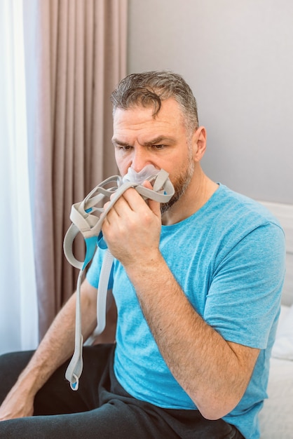 homme choqué malheureux avec des problèmes respiratoires chroniques surpris par l'utilisation d'une machine cpap assis sur le lit