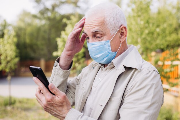 Homme choqué avec masque médical à l'aide du téléphone pour rechercher des nouvelles