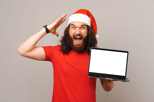 Un homme choqué montre une offre de Noël sur un écran d'ordinateur portable qu'il tient