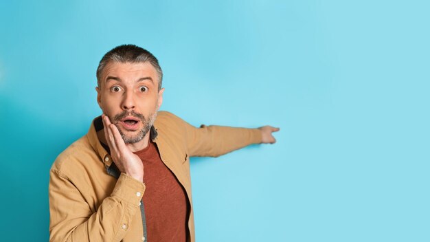 Homme choqué pointant le doigt de côté sur fond bleu espace vide