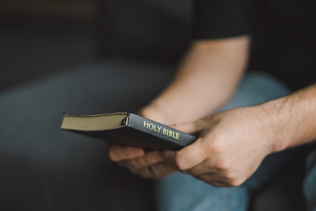 Un homme chrétien tient la sainte Bible dans ses mains en lisant la Sainte Bible dans une maison.