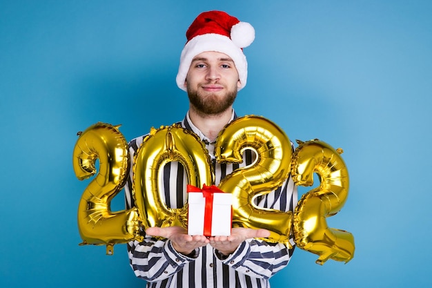 Un homme coiffé d'un chapeau de Noël tient les chiffres 2022 et un coffret cadeau