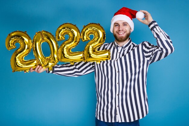 Un homme coiffé d'un chapeau de Noël tient les chiffres 2022 à partir de ballons gonflables