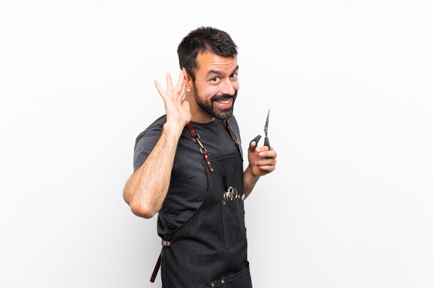 Homme de coiffeur dans un tablier écoutant quelque chose en mettant la main sur l'oreille