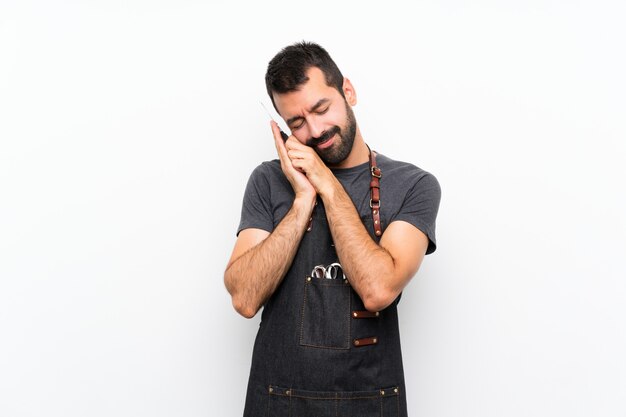 Homme coiffeur dans un tablier faisant un geste de sommeil dans une expression dorable