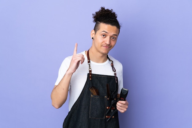 Homme de coiffeur dans un tablier sur mur violet isolé pointant avec l'index une excellente idée