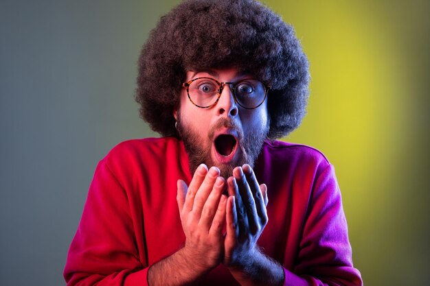 Homme avec une coiffure afro regardant la caméra avec un visage choqué et de grands yeux et une bouche ouverte