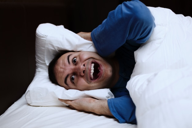 Photo homme en colère à l'aide d'un oreiller pour couvrir ses oreilles