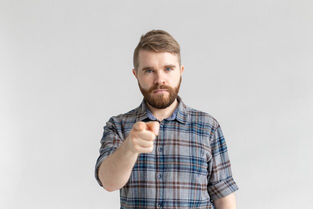 Homme en colère avec barbe, doigt pointé vers la caméra sur fond blanc