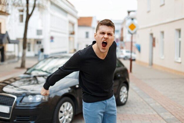 Un homme en colère crie près d'une voiture dans la ville. Le concept de colère