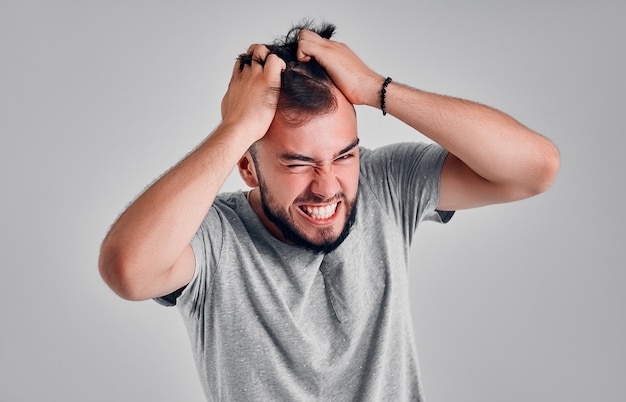 Homme en colère et furieux sur fond gris. Il s'arrache les cheveux de rage