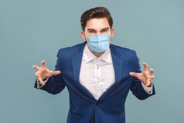 Homme en colère avec masque médical chirurgical en costume bleu regardant la caméra