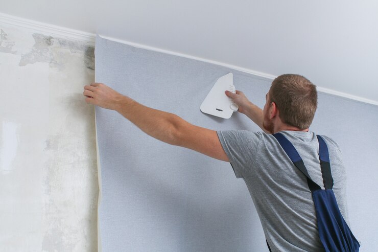 Un homme colle du papier peint en vinyle gris sur un support non tissé. Rénovation de la salle.